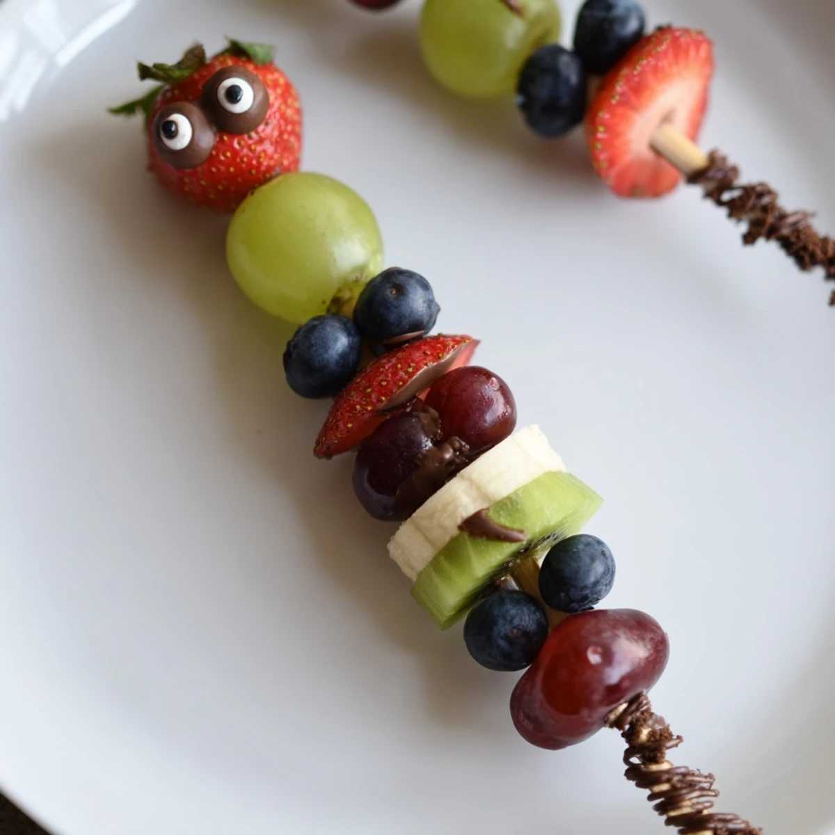 Colorful caterpillar fruit skewer track with fresh grapes, strawberries, and a fun cookie crumb path.