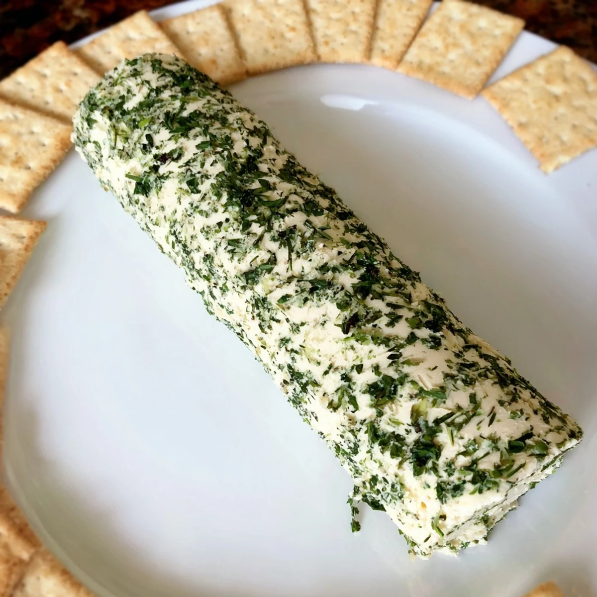 A close-up shot of the Herb-Coated Cheese Log, seasoned with fresh herbs, offering a delightful appetizer.