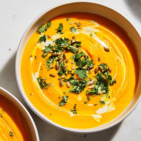 Creamy, vibrant Sweet Potato & Carrot Soup served in a bowl, garnished with fresh herbs and seeds.
