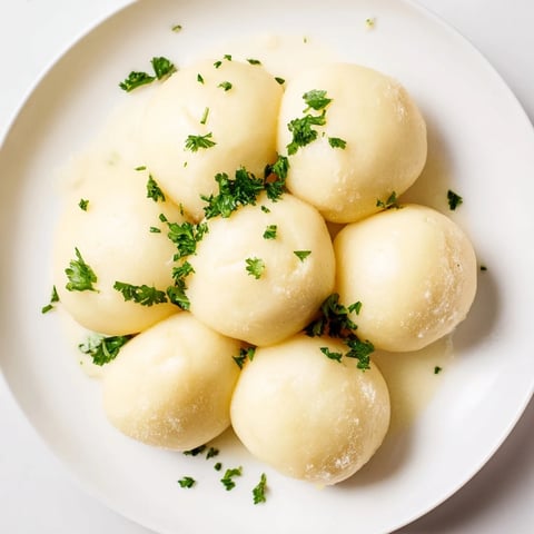 Fluffy, golden brown potato dumplings, ready to serve with savory gravy on a white plate.