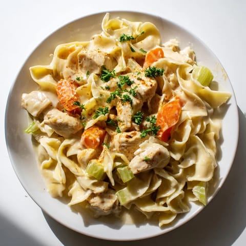 A steaming bowl of Creamy Chicken and Egg Noodles, with visible herbs and vegetables, looks inviting.