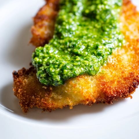 Crispy Pesto Chicken Cutlets with a juicy interior, drizzled with bright green pesto beside a glass of white wine.  