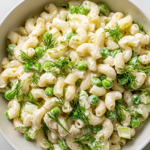A close-up of Creamy Dill Pickle Pasta Salad with ditalini, diced pickles, and green peas in a creamy dressing.