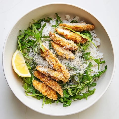 Goldene, knusprige Parmesanschnitzel auf fluffyem Reis mit frischem Rucola und Zitrone – ein leichter Crispy Parmesan Chicken Cutlet Bowl.