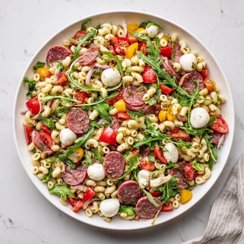 Ein buntes Frühjahr-Antipasto-Pastasalat mit Ditalini, Salami, Mozzarella und Arugula im Glas.